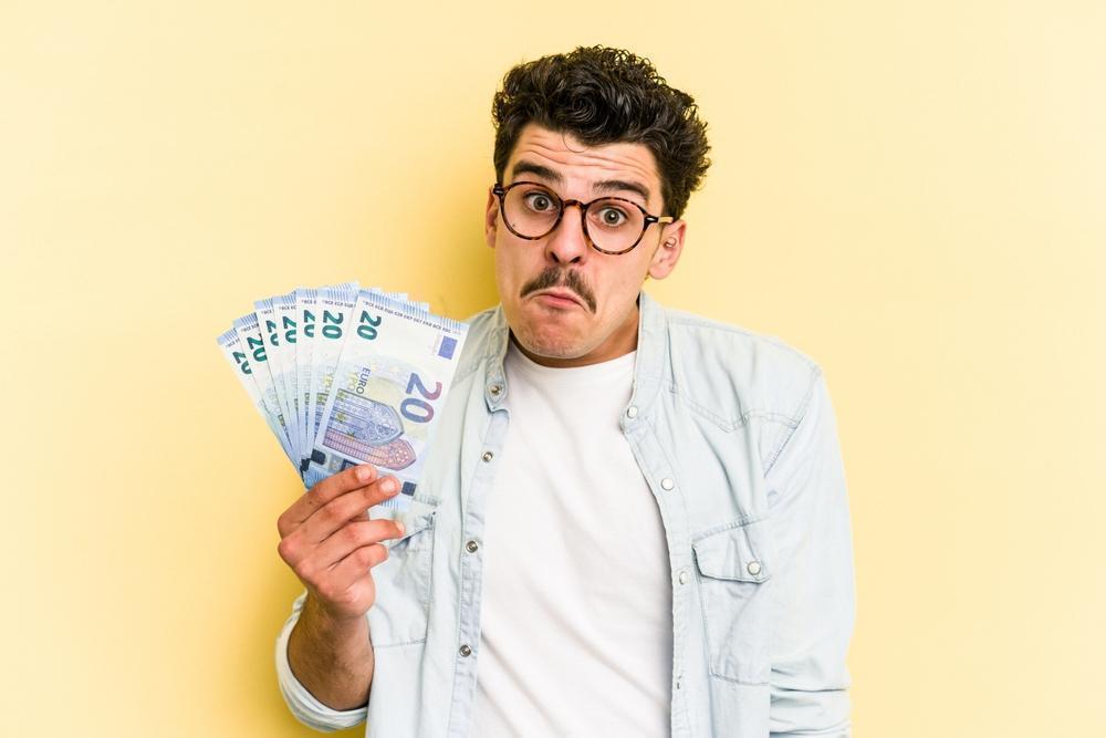 Young,Caucasian,Man,Holding,Banknotes,Isolated,On,Yellow,Background,Shrugs