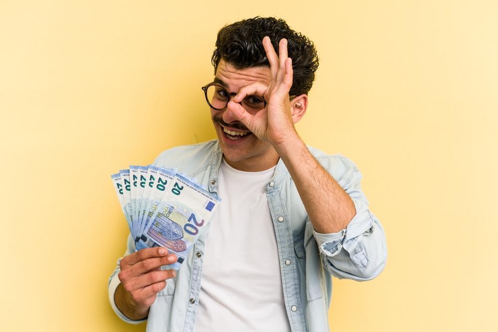 Young,Caucasian,Man,Holding,Banknotes,Isolated,On,Yellow,Background,Excited